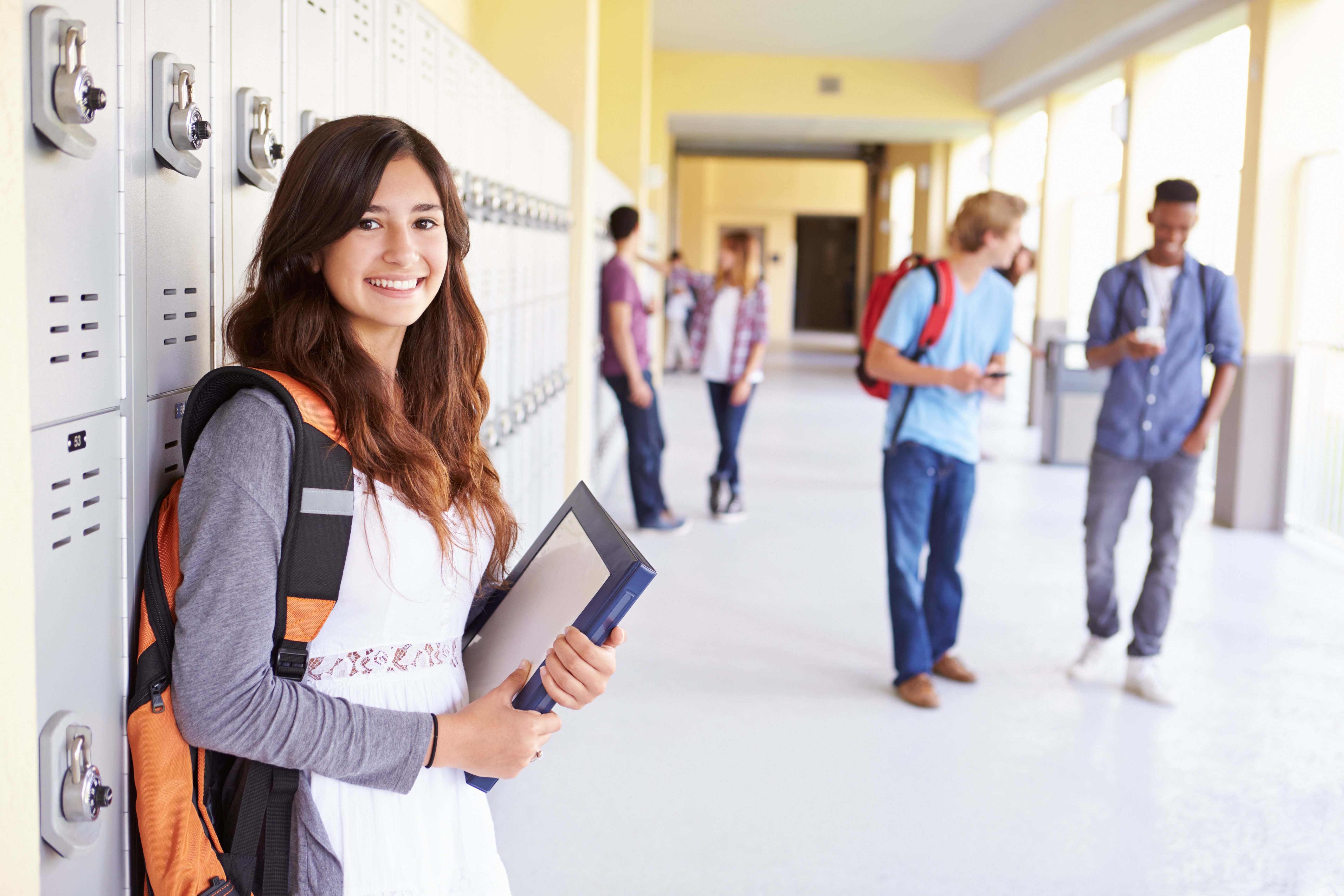 High school girl leaning against locker in crowded school hallway